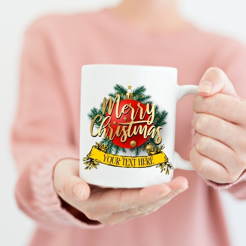 Ceramic Christmas mug featuring a red bauble in front of pine needles with 'Merry Christmas' in gold script, ideal for festive holiday beverages.